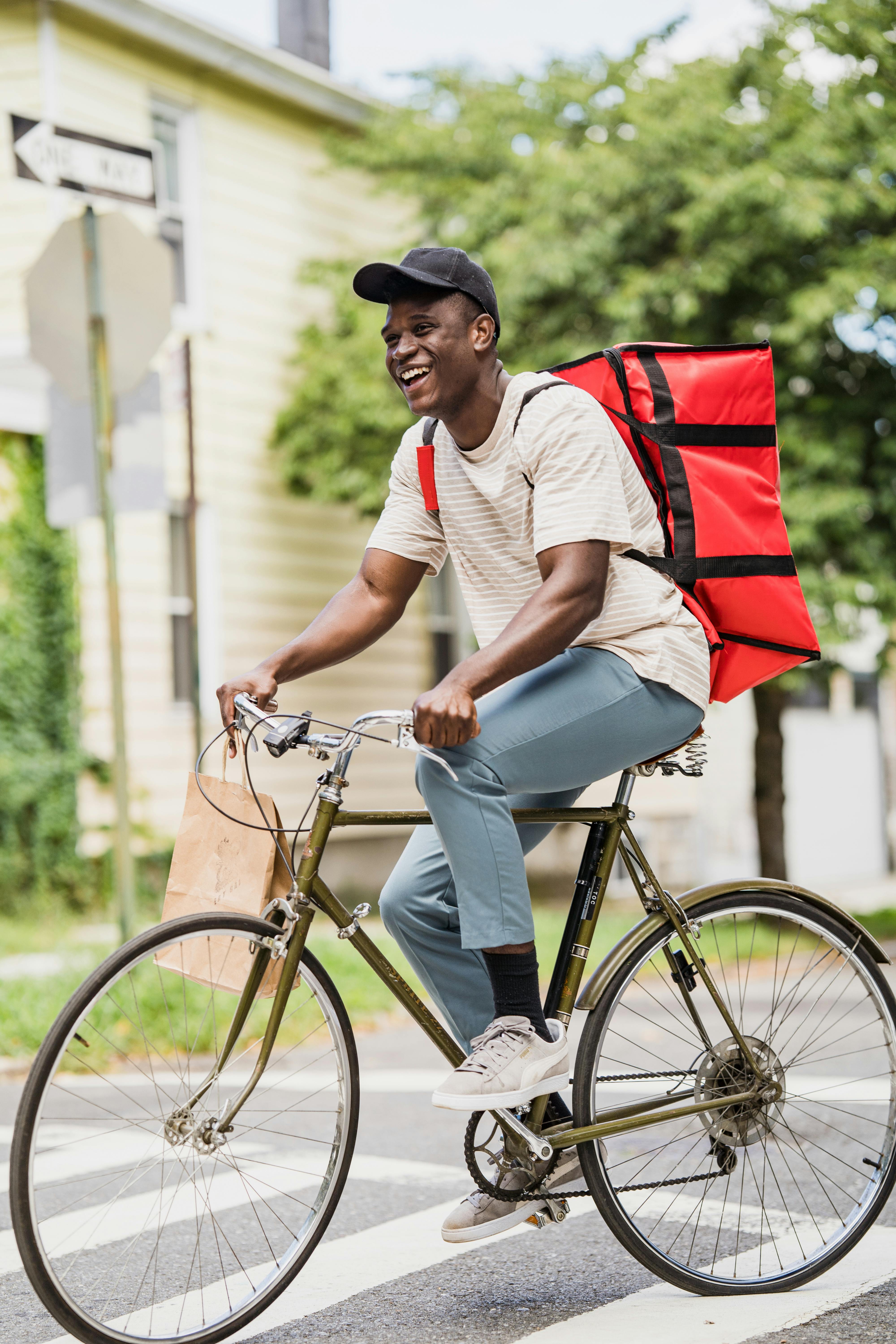 A courier smiles while delivering packages on a bicycle in an urban setting.