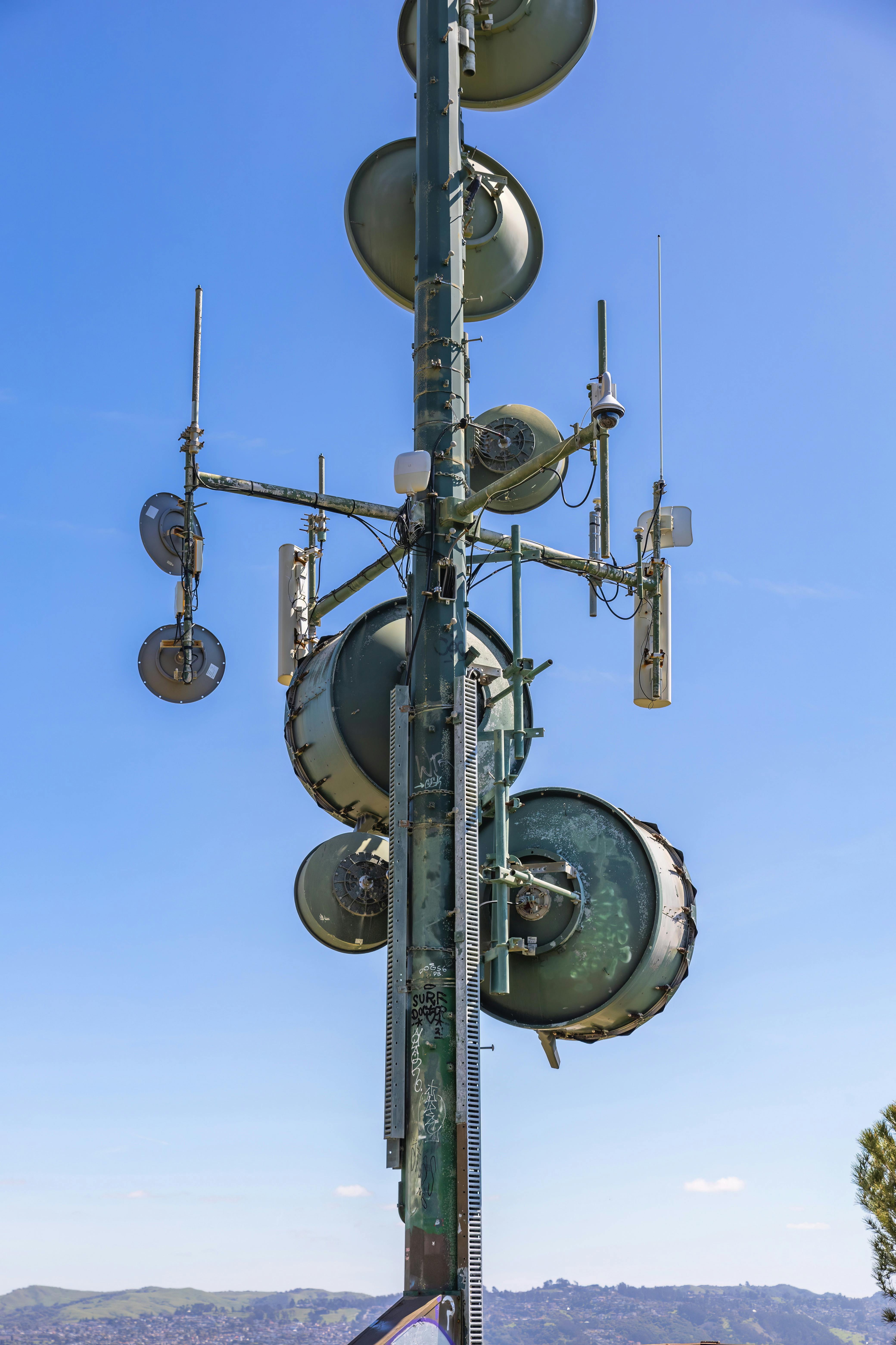 Vertical shot of a communication tower with multiple satellite dishes against a clear blue sky.