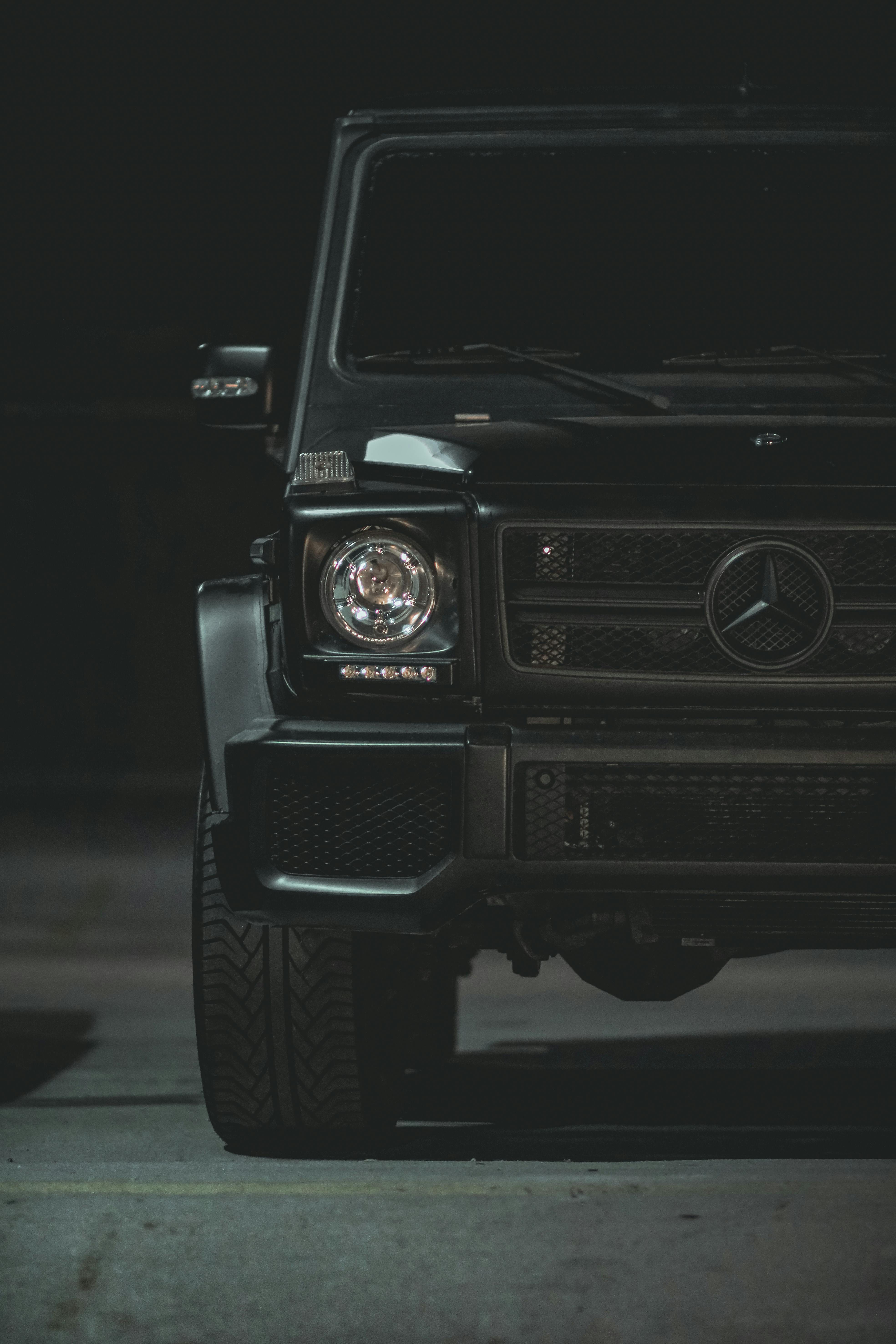 Close-up of a luxury black car's front, featuring a sleek design and emblem under nighttime lighting.